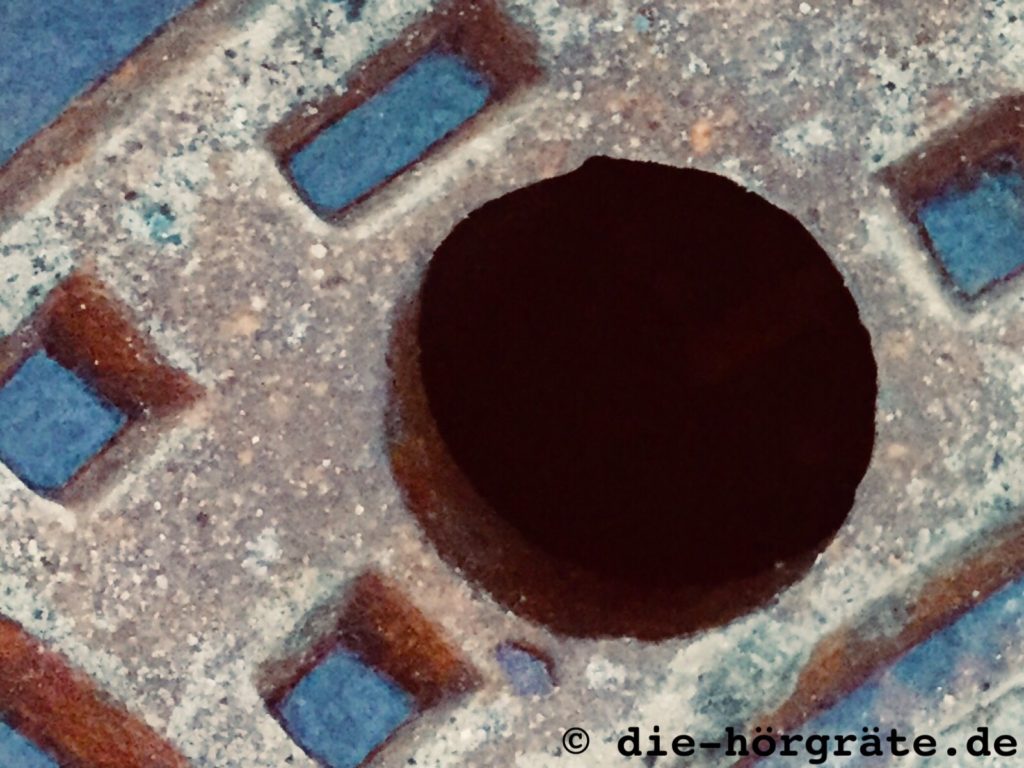 ein kleines Stück von einem alten, gusseisernen Kanaldeckel, vor allem ein Loch, durch das man ins Dunkel blicken kann